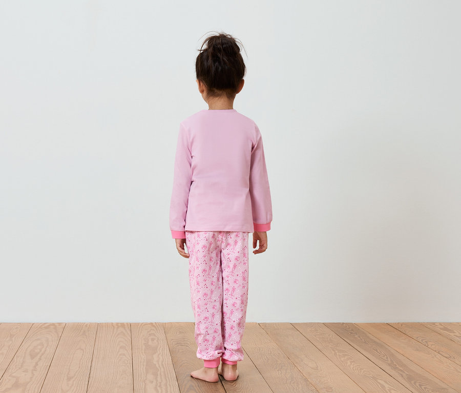 Dievča v ružovom pyžame stojí chrbtom k fotoaparátu.