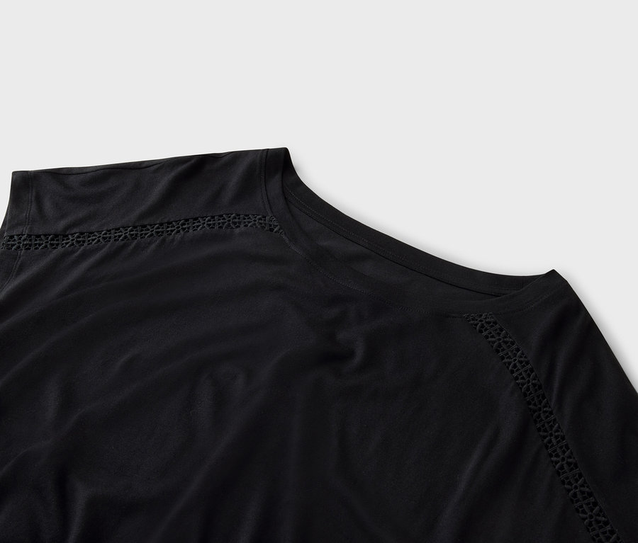 Detailný záber na čierny top s dierkovanou výšivkou pozdĺž výstrihu.