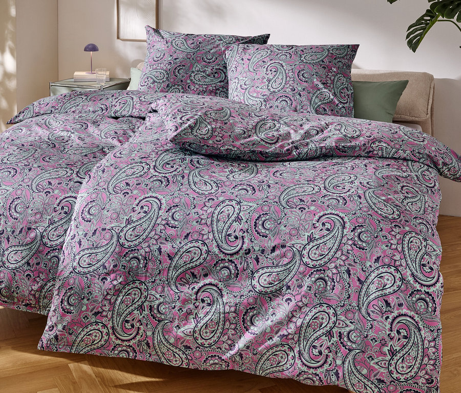 Detailný záber na posteľ s ružovou posteľnou bielizňou s paisley vzorom.