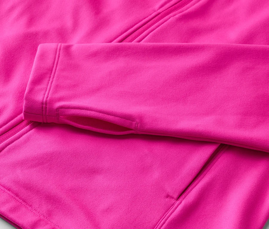 Detail ružovej fleecovej bundy so zipsom a otvormi na palce na rukáve.