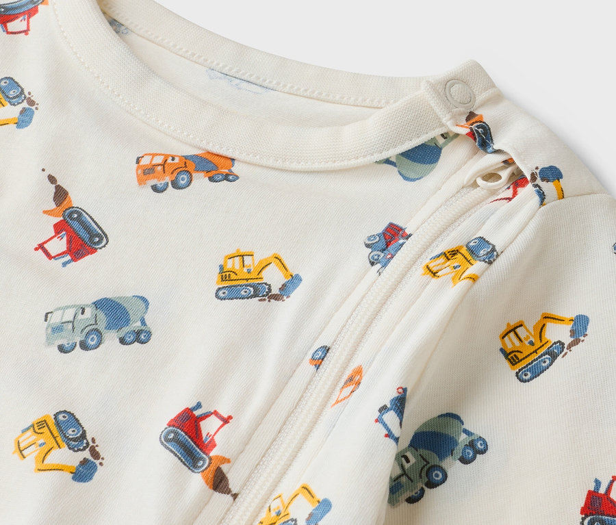 Detailný záber krémového dojčenského overalu so zipsom a vzorom stavebných vozidiel.