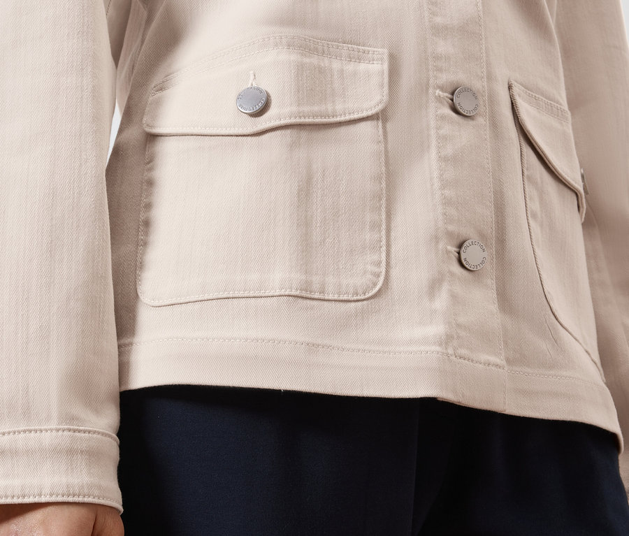 Detailný záber na svetlohnedú džínsovú bundu so striebornými gombíkmi a našitými vreckami.