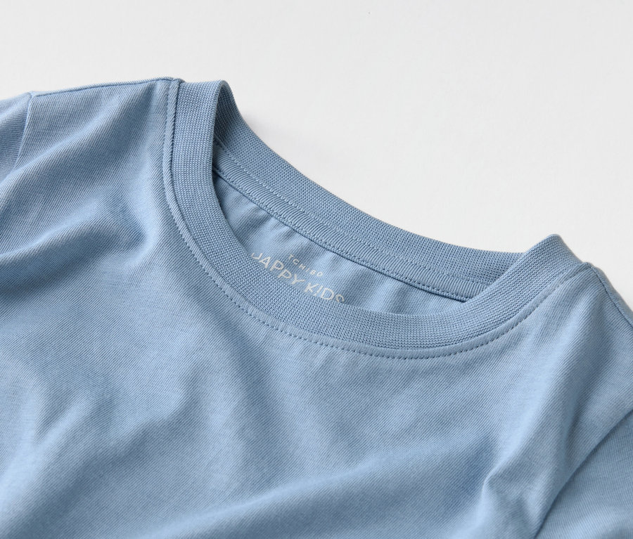 Detailný záber svetlomodrého trička s nápisom "JAPPY KIDS" na golieri.