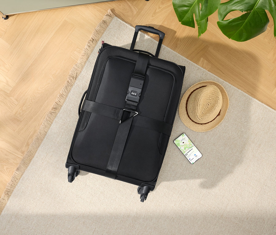 Čierny kufor na kolieskach s klobúkom a smartfónom na béžovom koberci.