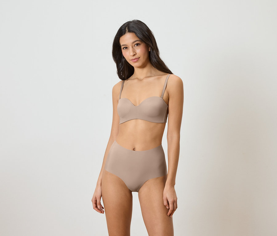 Žena má na sebe béžovú podprsenku bez ramienok a nohavičky s vysokým pásom.