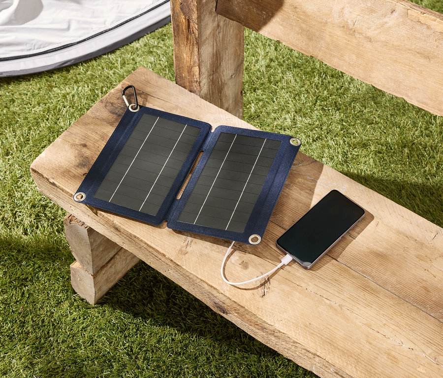 Solárny panel nabíja smartfón na drevenej lavici vonku.