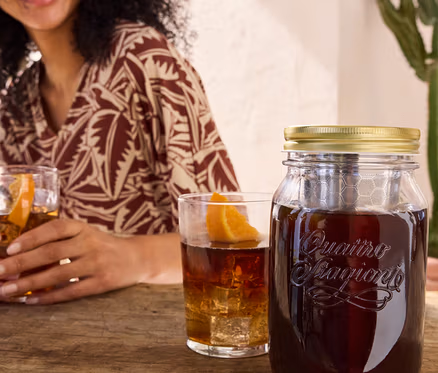 Žena drží pohár s nápojom vedľa pohára na studenú kávu cold brew »BrewJar« a džersejových šiat s potlačou.