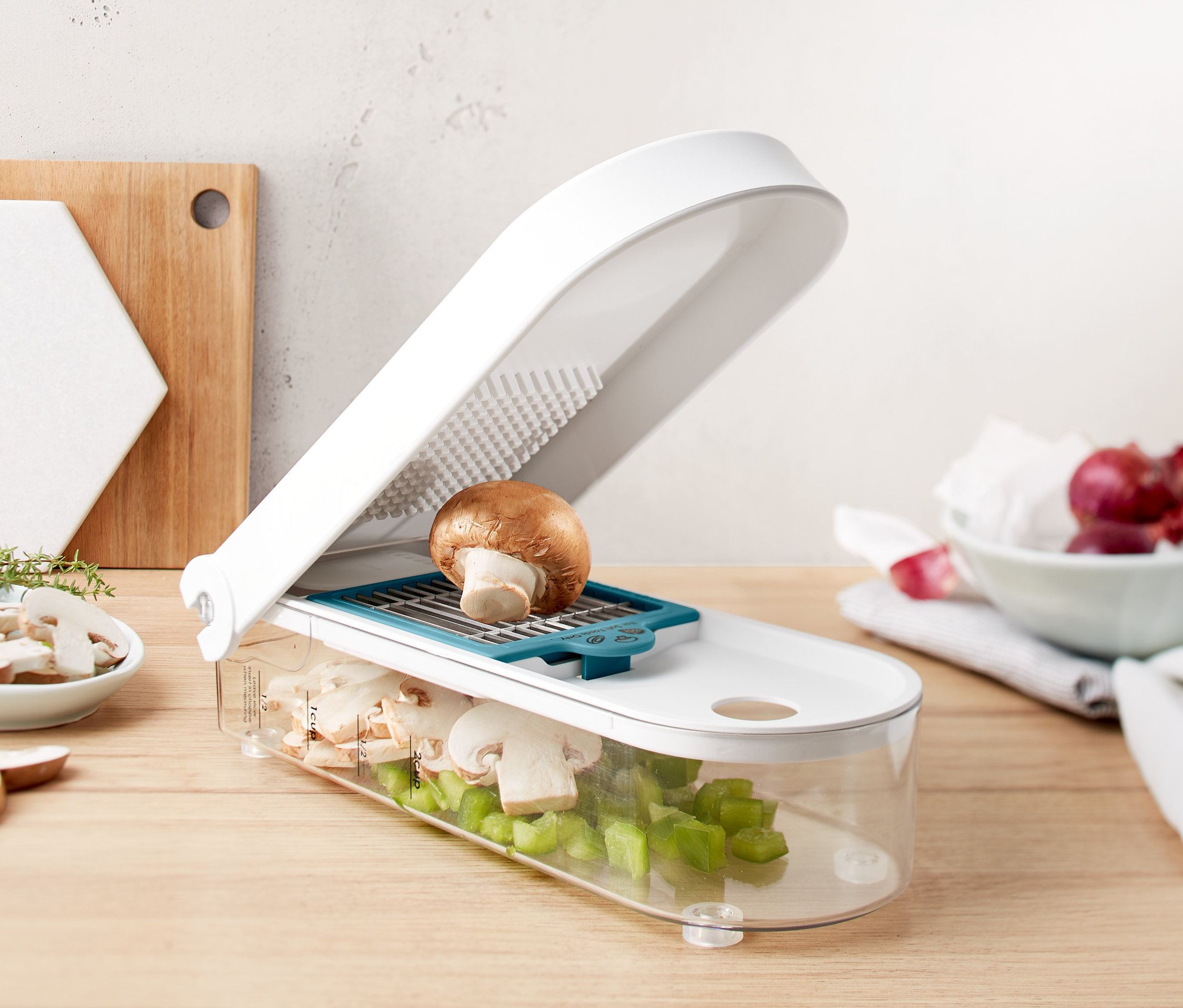 Hnedá huba na bielom krájači na ovocie a zeleninu s priehľadnou nádobou plnou nakrájaných húb a zelenej papriky.