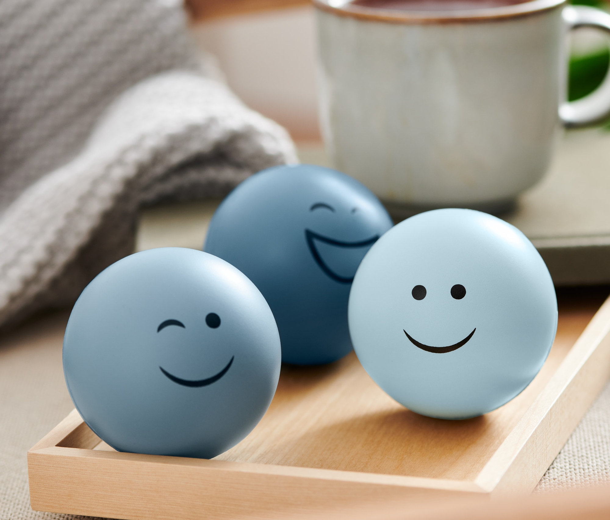 Tri antistresové loptičky s tvárami na drevenom podnose.