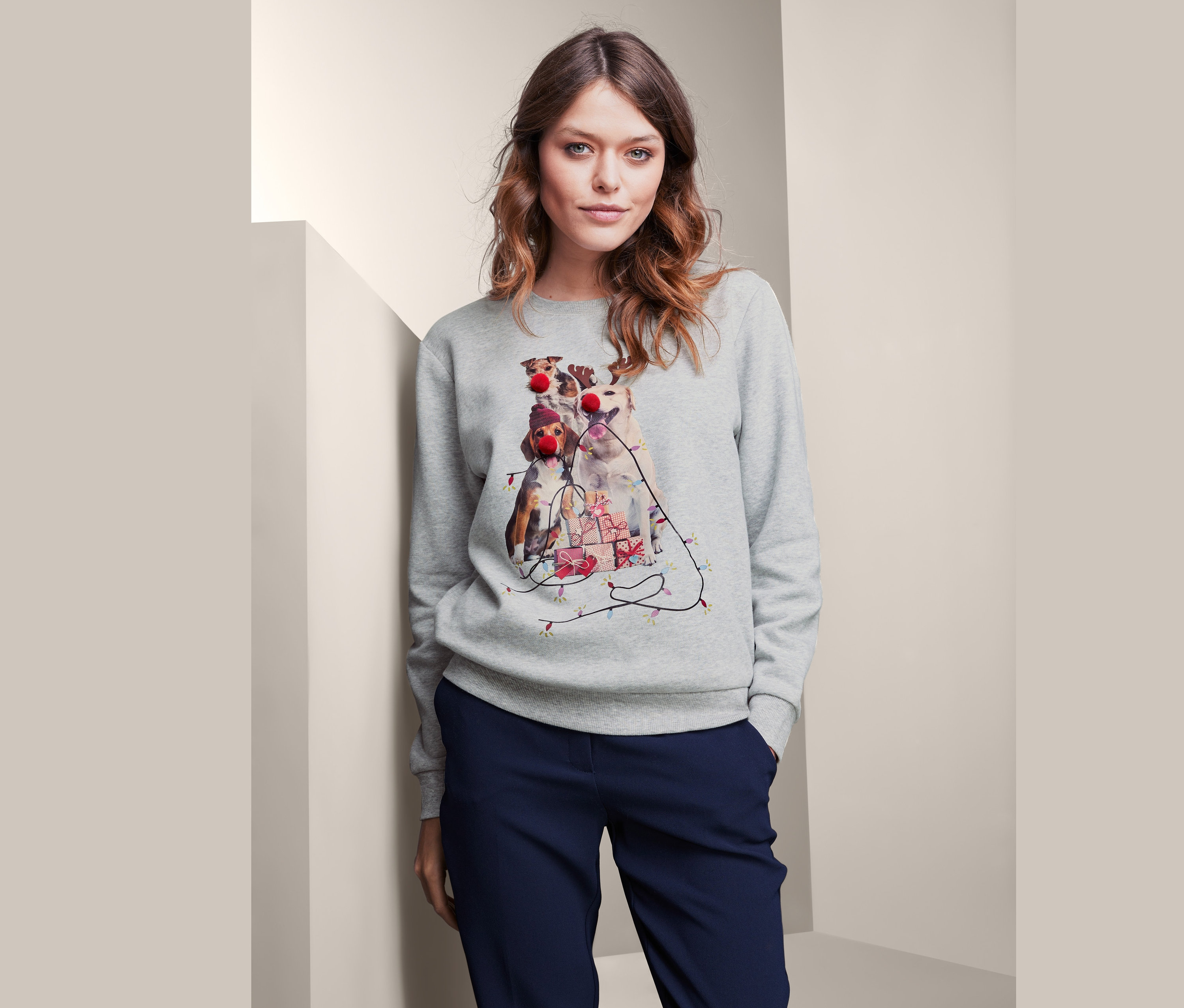 Žena má na sebe sivú mikinu s potlačou psov s vianočnou tematikou.