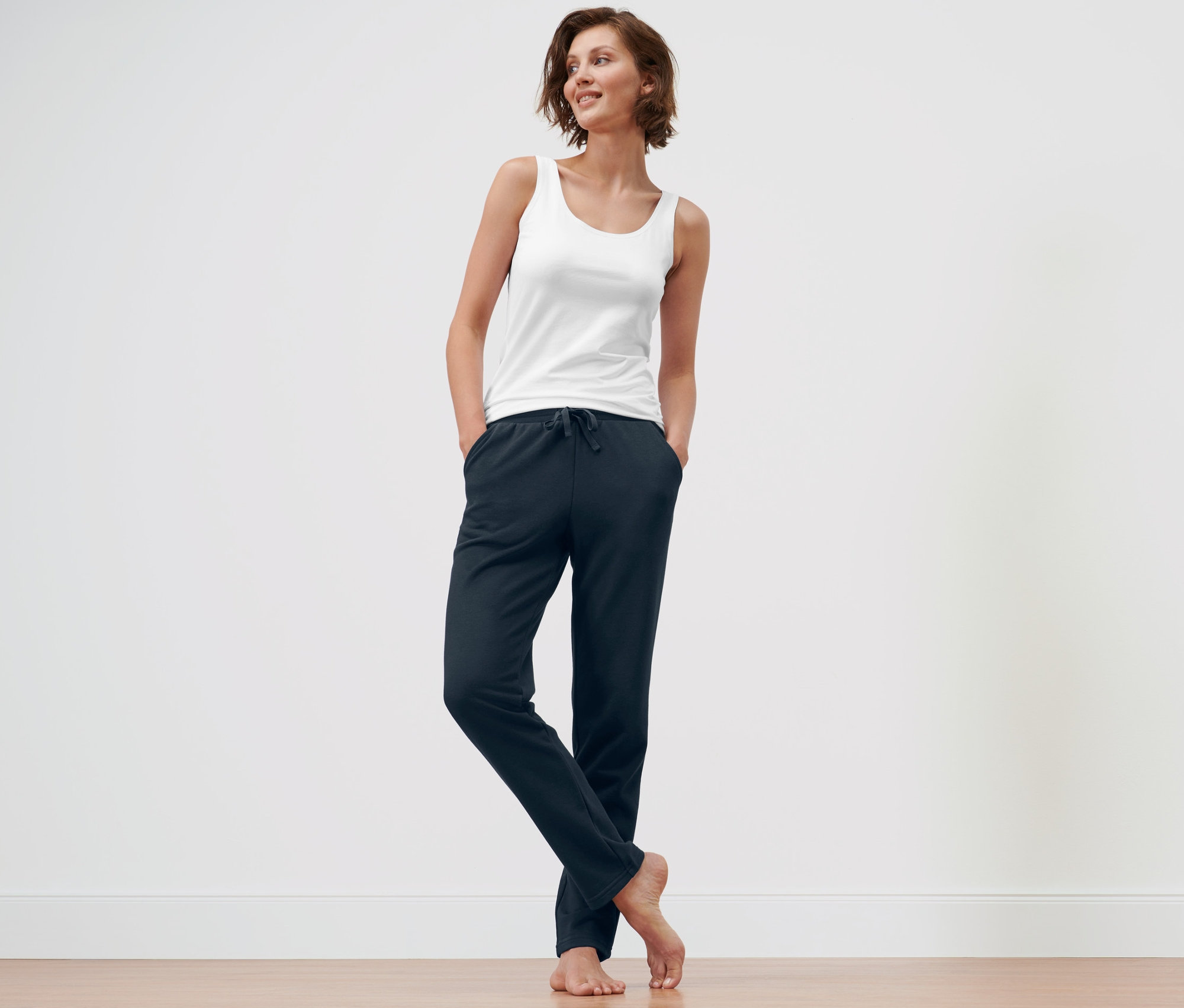 Žena stojí a má ruky vo vreckách tmavomodrých domácich nohavíc a modrých domácich nohavíc.