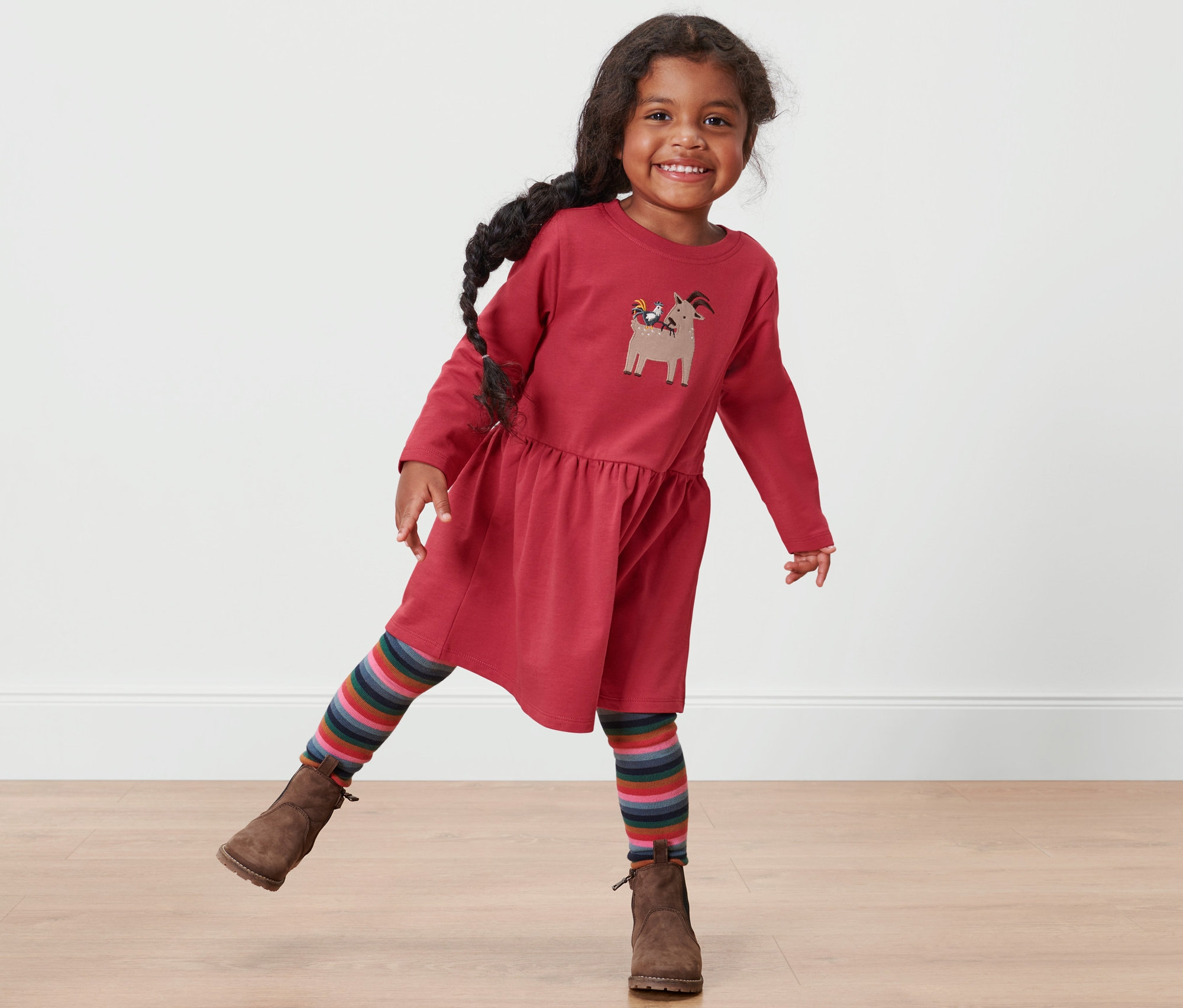 Usmievajúce sa dievčatko pózuje v červených teplákových šatách.