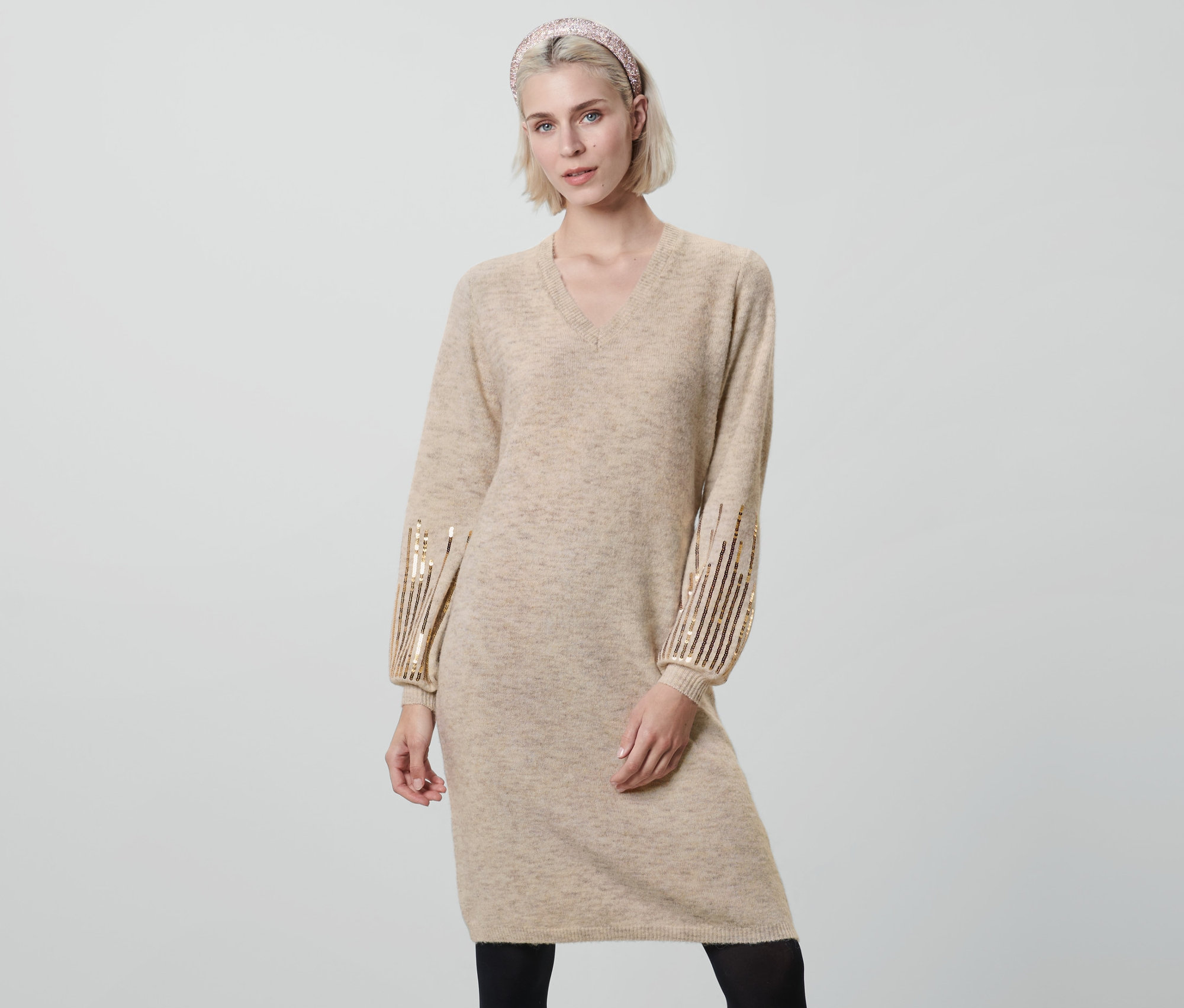 Žena pózuje v béžových úpletových šatách s flitrami.