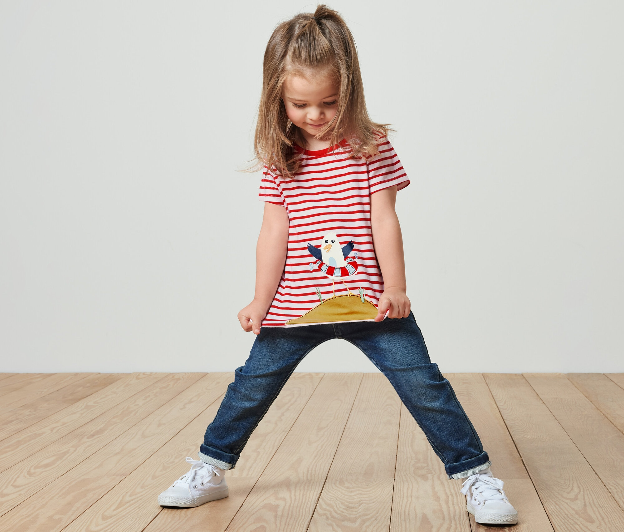 Dievča stojí a drží si okraj trička s červenými pruhmi a aplikáciou.