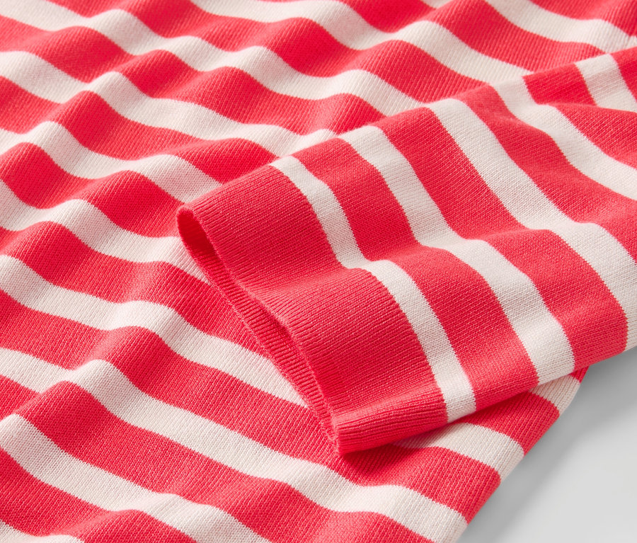 Detail pruhovaného pulóvra z jemného úpletu s červeno-bielymi pruhmi.