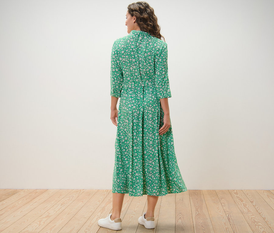 Žena stojí chrbtom ku kamere a má na sebe zelené košeľové šaty s potlačou.