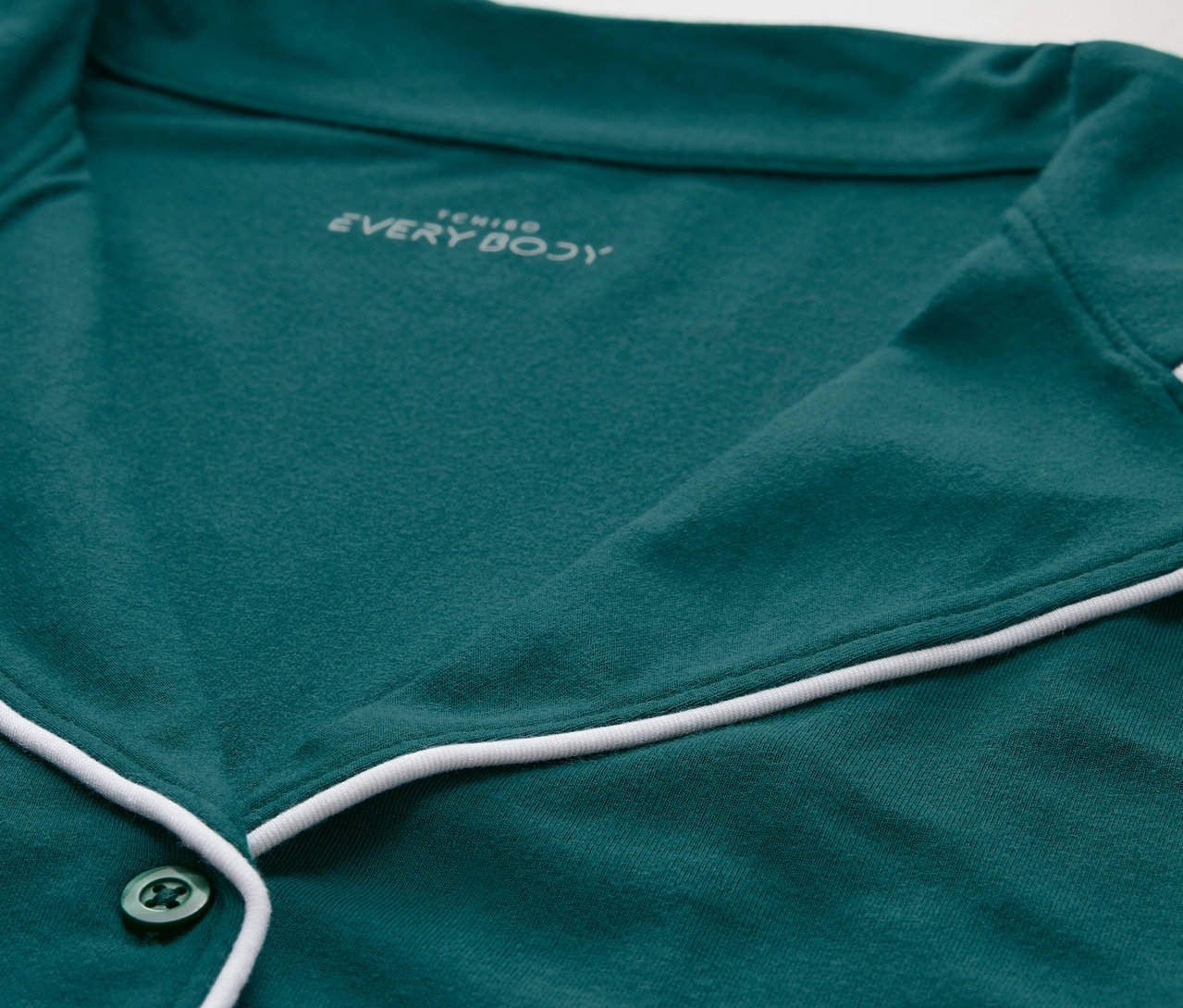 Detail zeleného pyžamového topu s bielym lemovaním a gombíkmi.