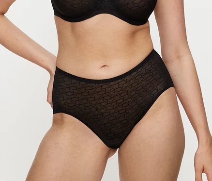 Osoba v čiernych nohavičkách Triumph Signature Sheer Maxi EX z vzorovaného materiálu a zladenom podprsenke, s rukami na bokoch.