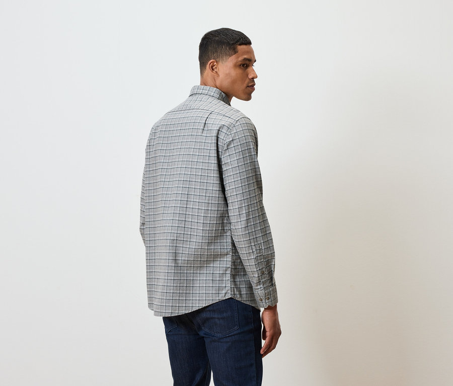 Muž v kockovanej košeli a tmavých džínsoch stojí chrbtom k divákovi.