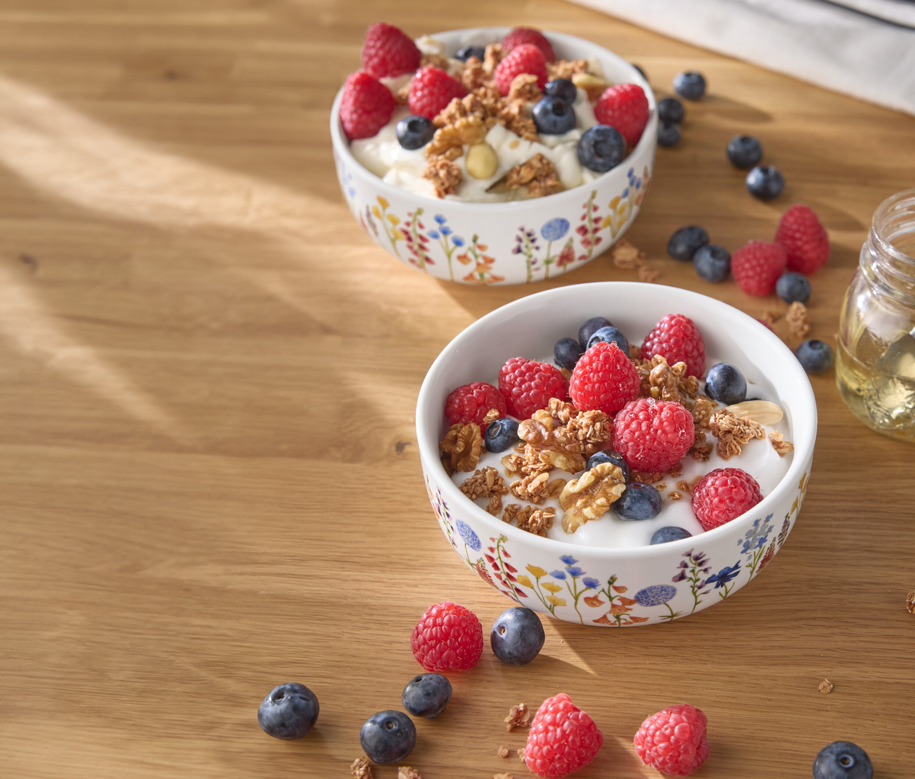 Dve misky jogurtu s malinami, čučoriedkami a orechmi na drevenom stole.