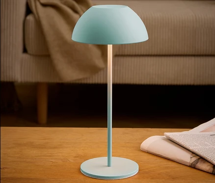 Tyrkysová lampa stojí na stole vedľa novín.