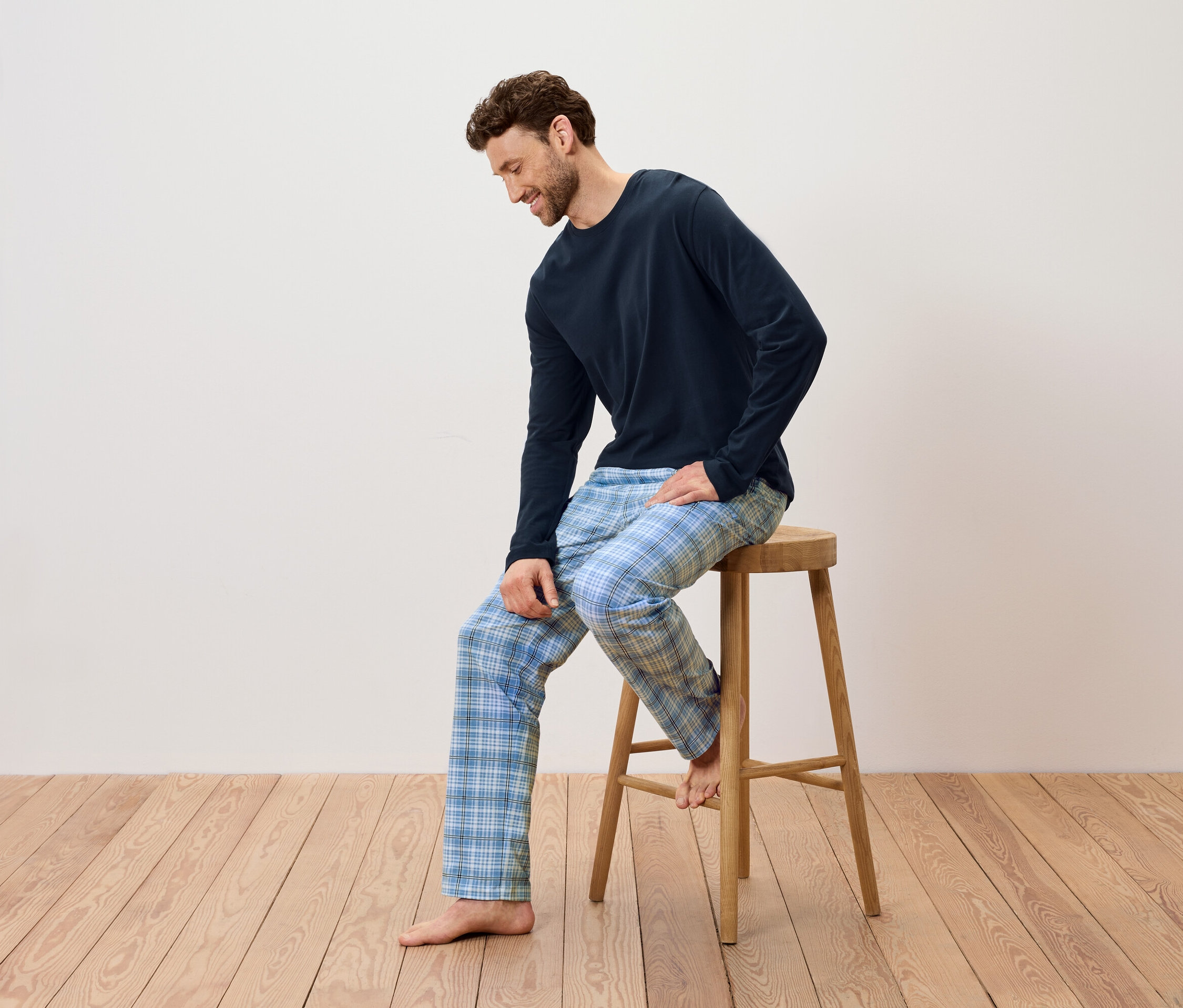 Muž sedí na drevenej stoličke, má na sebe tmavomodré pyžamo a modré kockované nohavice.