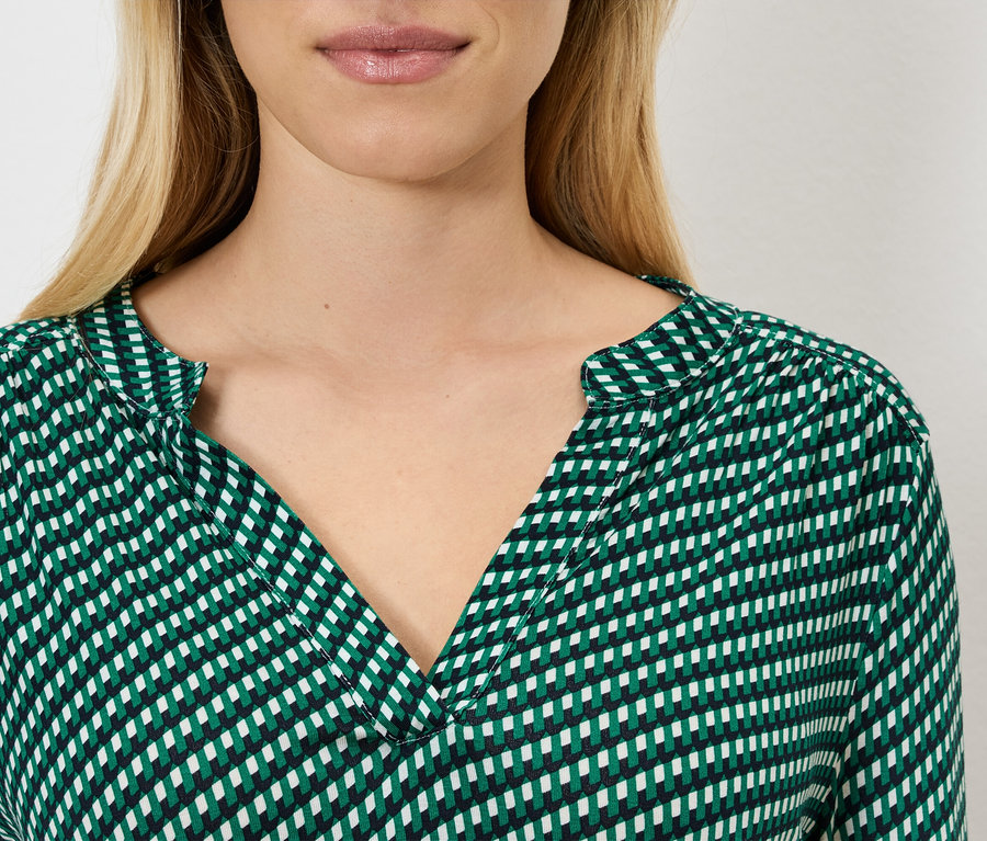 Detail ženy s blond vlasmi v zeleno-bielej blúzke.