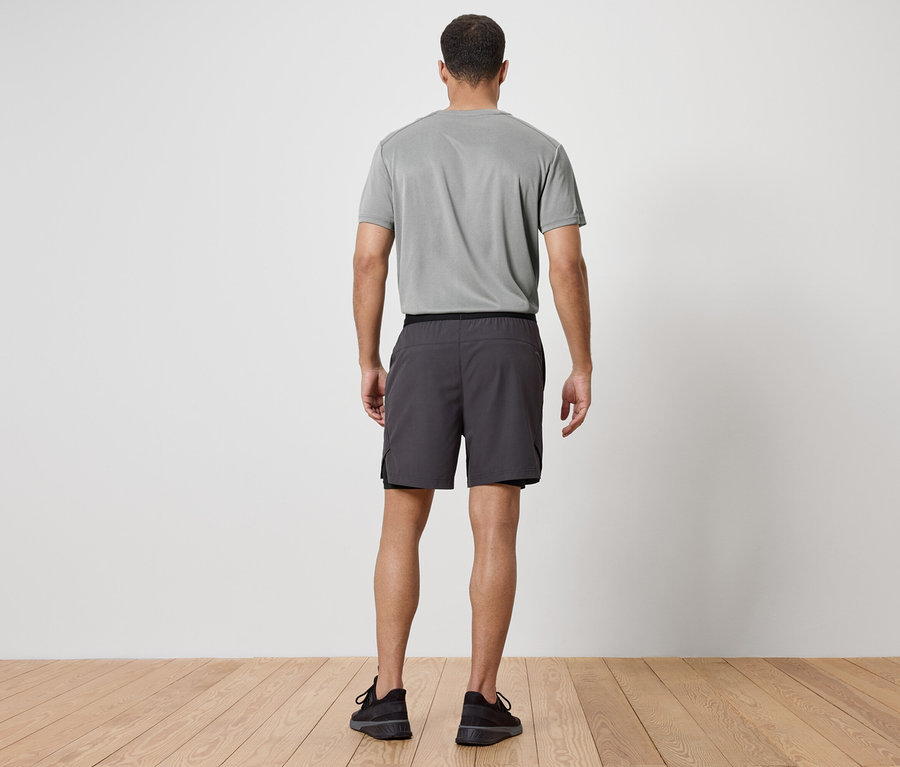 Muž chrbtom k fotoaparátu má na sebe sivé tričko, sivé šortky a čierne tenisky.