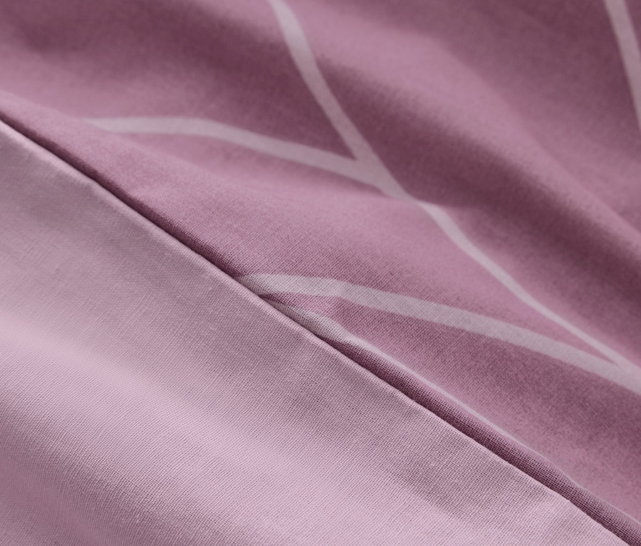 Detail fialovej posteľnej bielizne s bielymi geometrickými vzormi.