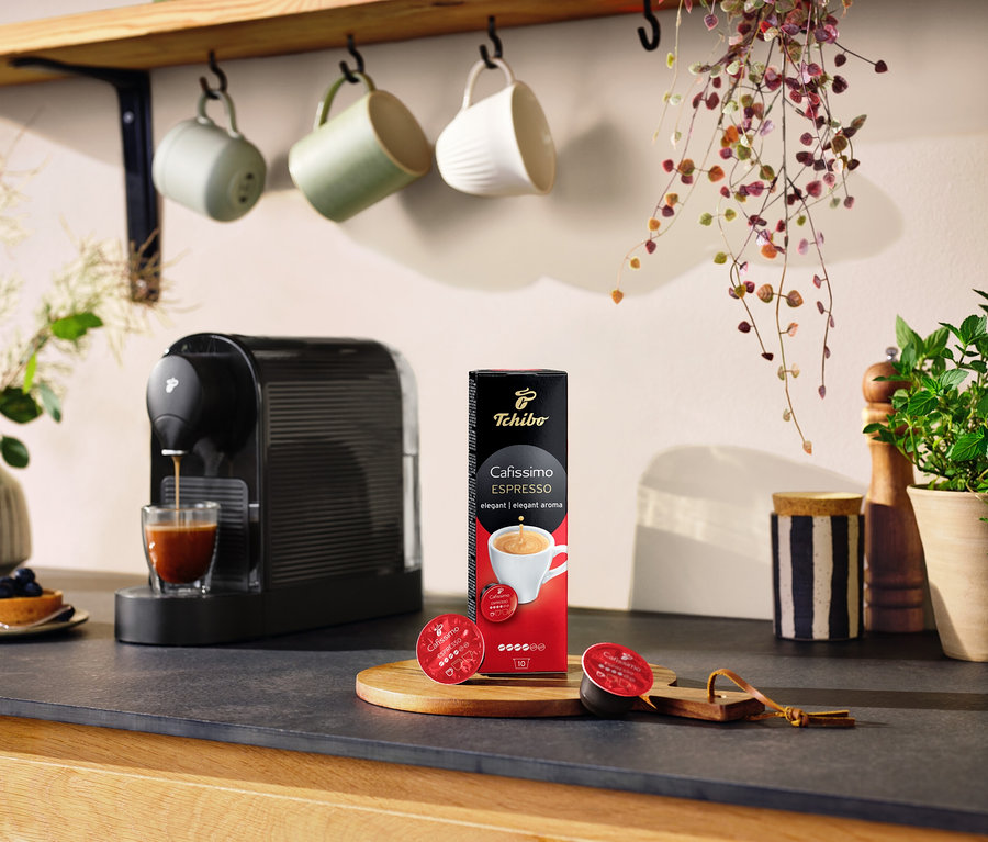 Espresso stroj naleje kávu do pohára vedľa balenia Cafissimo Espresso elegantné, 10 kapsúl.