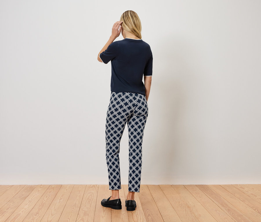 Žena stojí chrbtom k fotoaparátu a má na sebe tmavomodrý top, vzorované nohavice a čierne topánky.