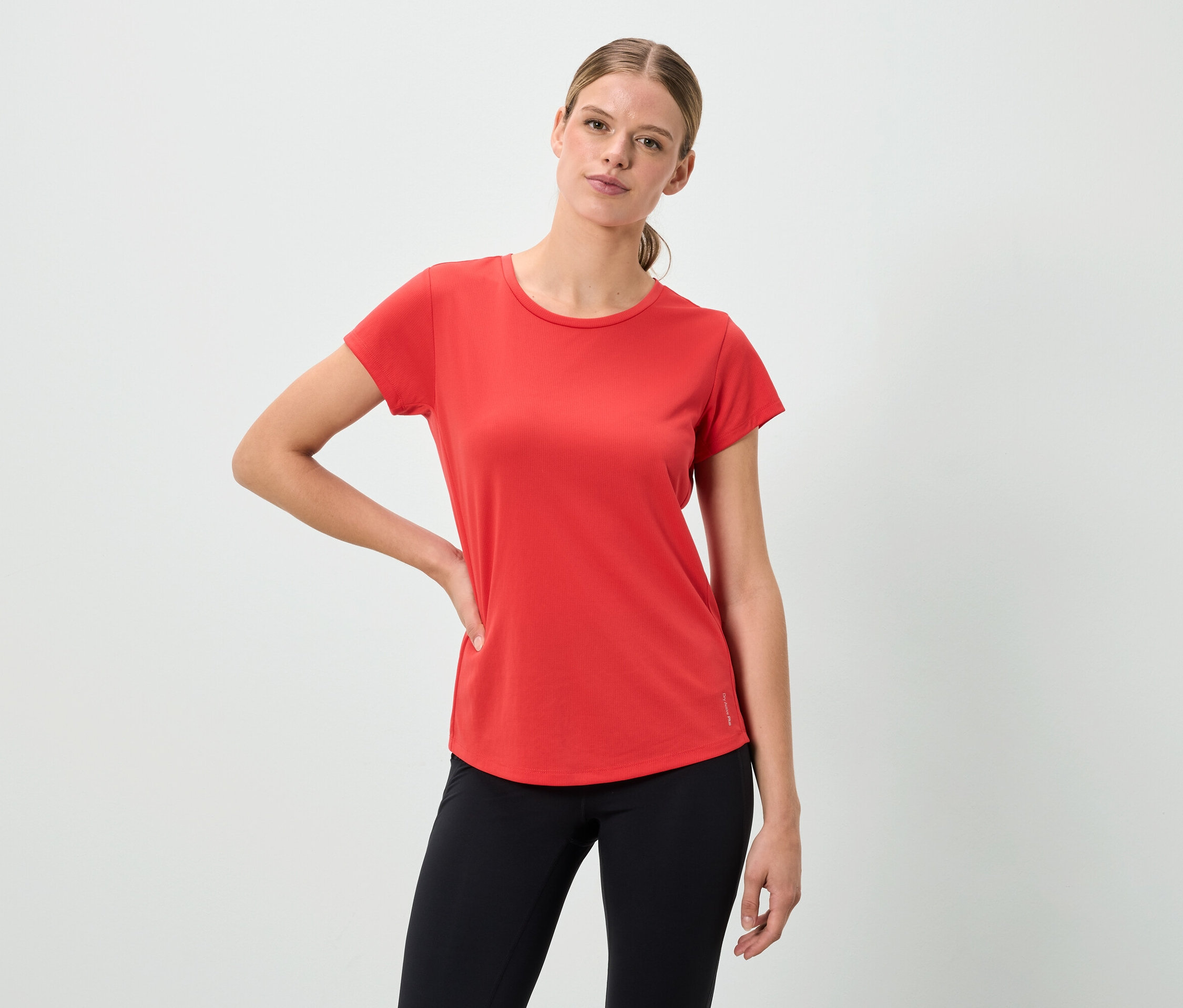 Žena pózuje v červenom tričku a čiernych legínach.