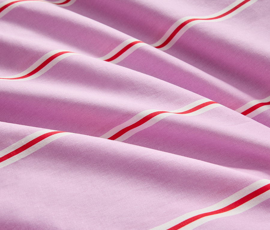 Detail záberu na zloženú ružovú látku s červenými a bielymi pruhmi.