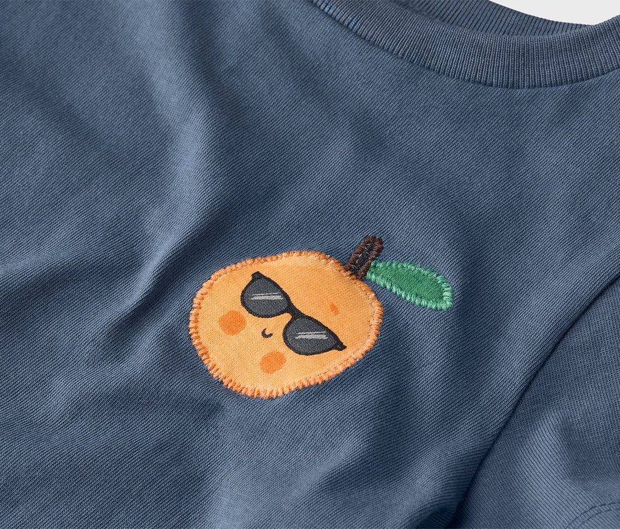 Detail modrého trička s našitou mandarínkou so slnečnými okuliarmi.