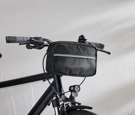 Detailný pohľad na čierny bicykel s čiernou taškou na riadidlá a svetlom na bicykel pred bielou stenou.