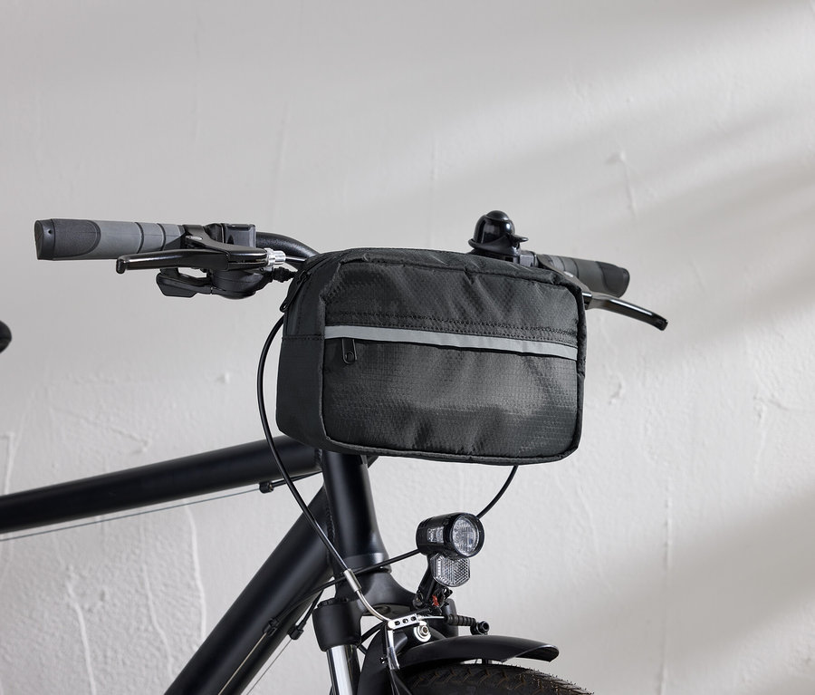 Detailný pohľad na čierny bicykel s čiernou taškou na riadidlá a svetlom na bicykel pred bielou stenou.