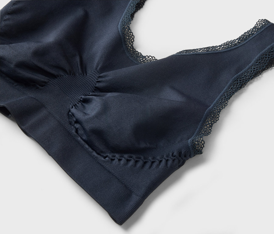 Detailný záber tmavomodrej podprsenky s čipkou na sivom pozadí.