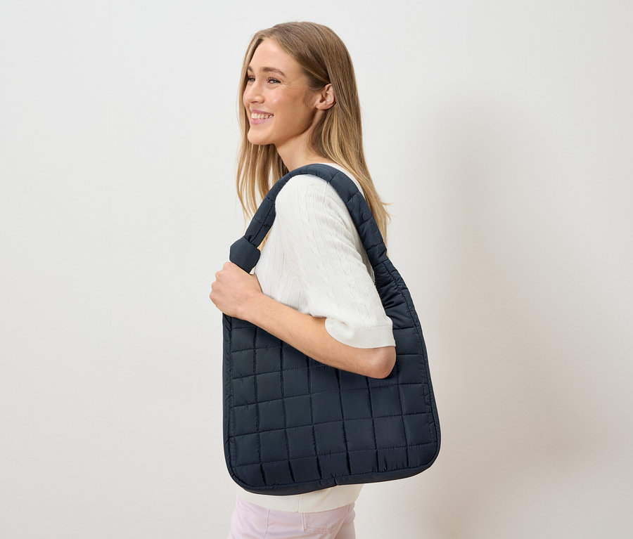 Žena nosí cez plece tmavomodrú, prešívanú tašku.