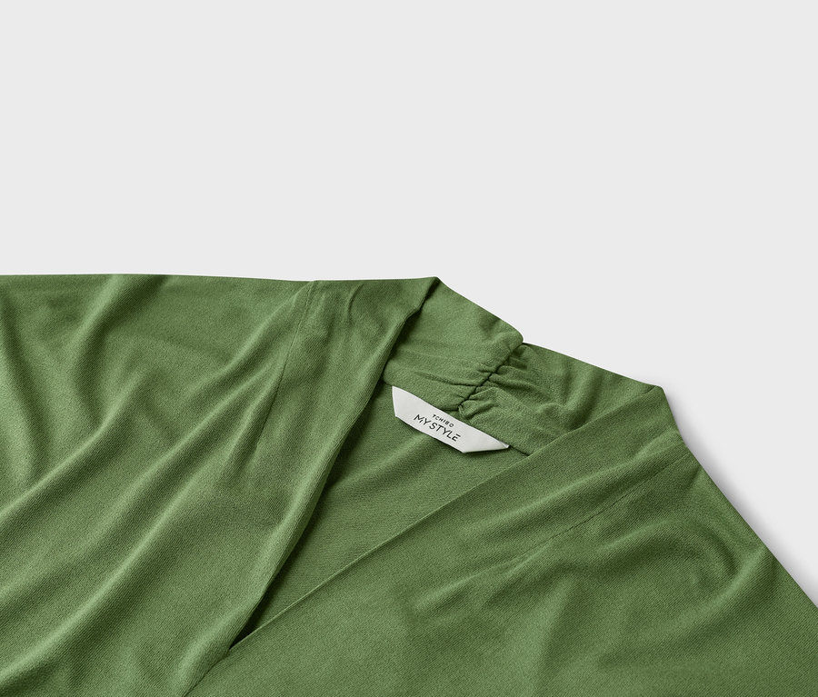 Detail zeleného prekladaného topu s výstrihom do V a štítkom s nápisom "TCHIRO MY STYLE".