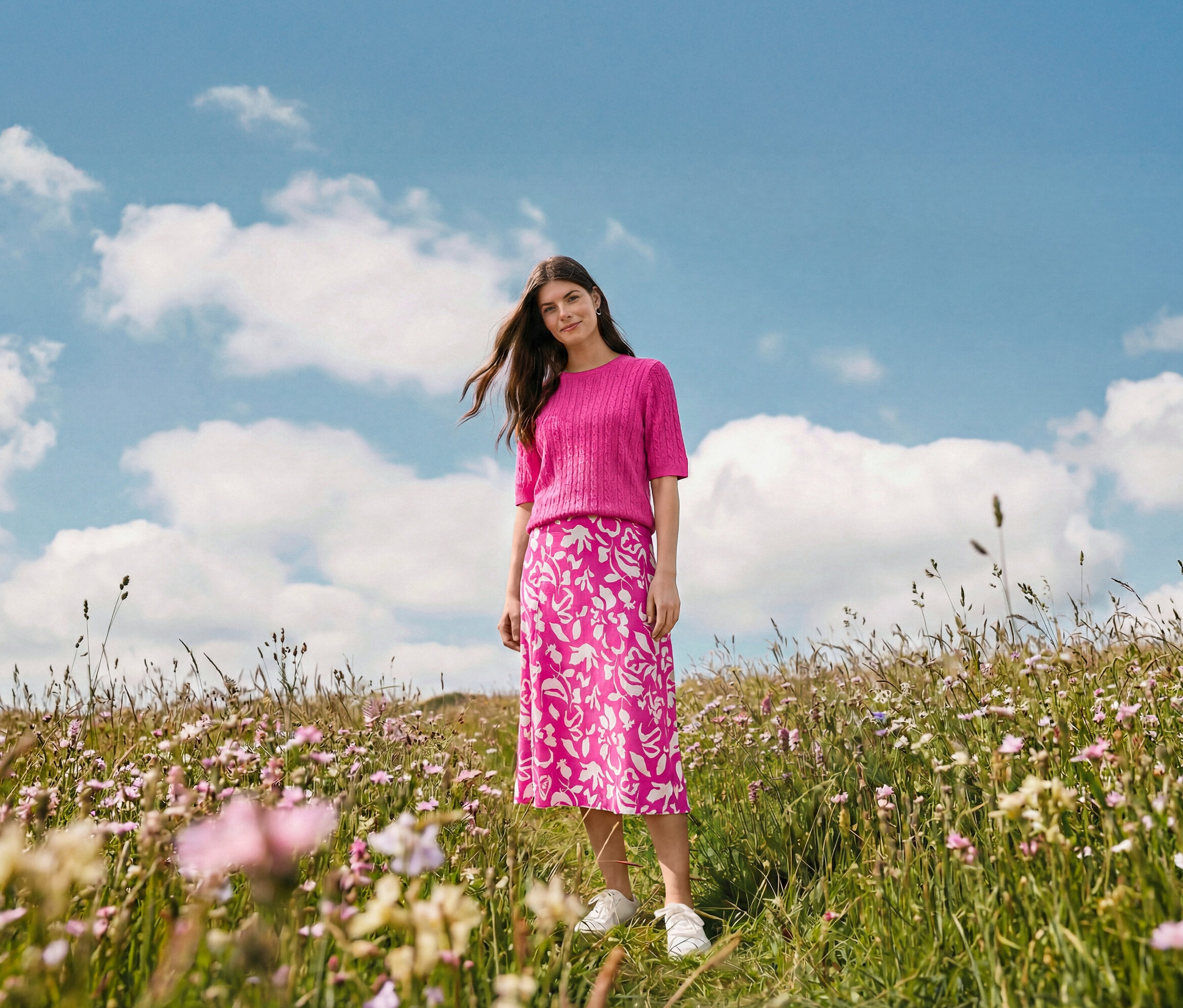 Žena stojí na lúke a má na sebe bedruckter midi-rock, kruhové náušnice Wave a kožené tenisky.