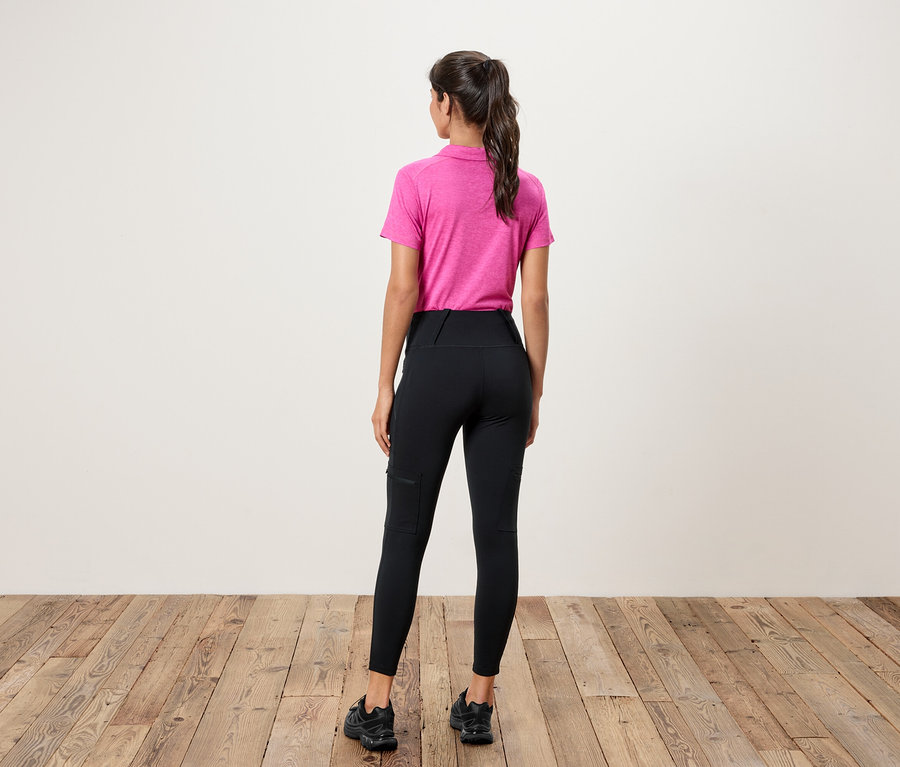 Žena stojí chrbtom k fotoaparátu a má na sebe ružové polo tričko a čierne legíny s vreckami.