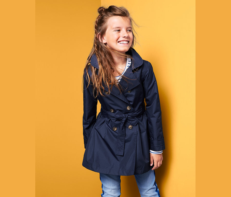 Usmievajúce sa dievča pózuje v tmavomodrom trenčkote do každého počasia.