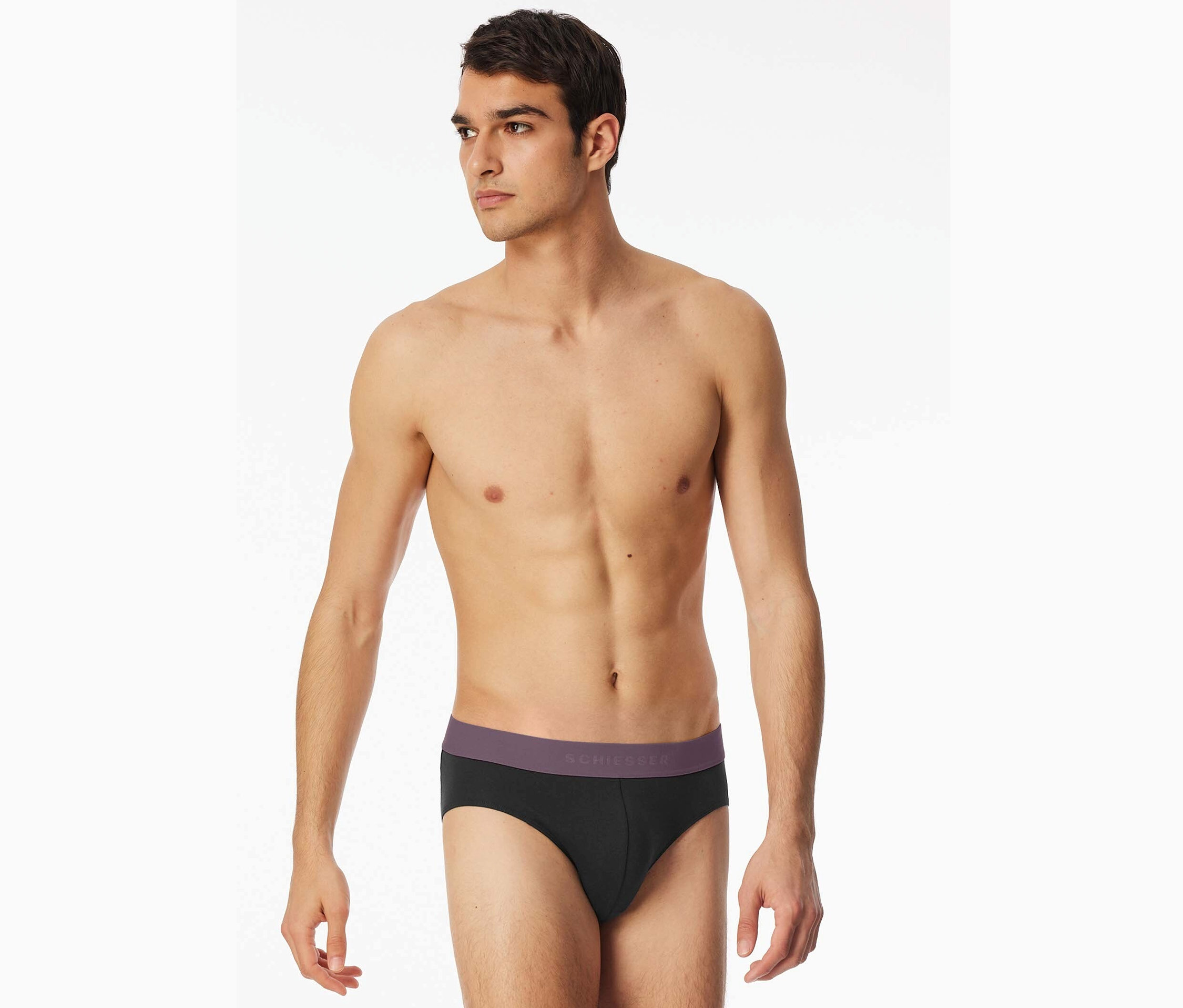 Muž s odhalenou hornou časťou tela nosí čierne slipy Schiesser s fialovým pásom.