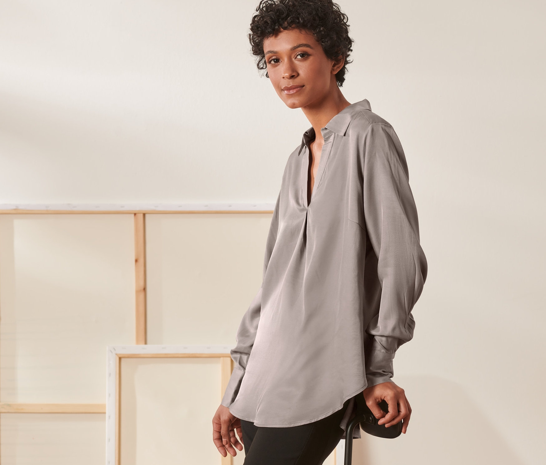 Žena opierajúca sa o stoličku má na sebe saténovú blúzku.