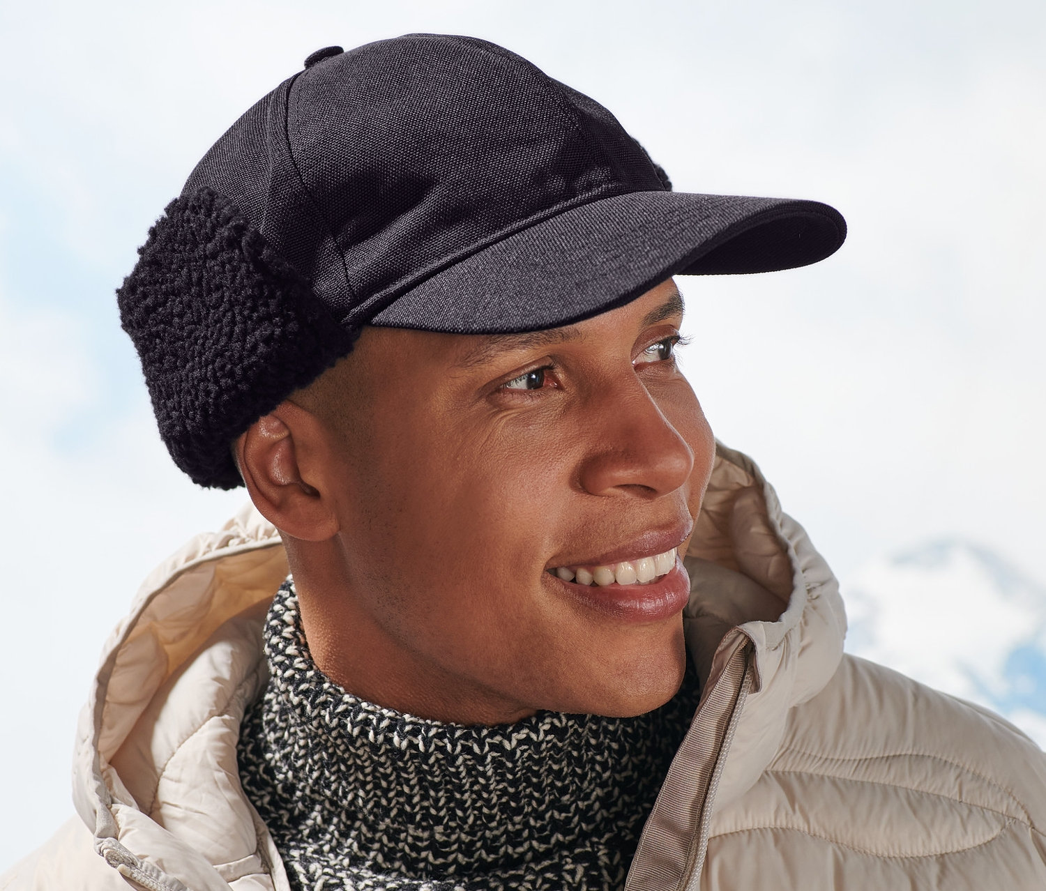 Muž sa usmieva a má na sebe béžovú bundu a funkčnú šiltovku.