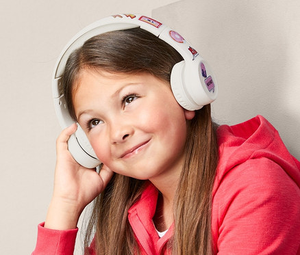 Dievča sedí a počúva hudbu cez bezdrôtové slúchadlá s Bluetooth® pre deti.