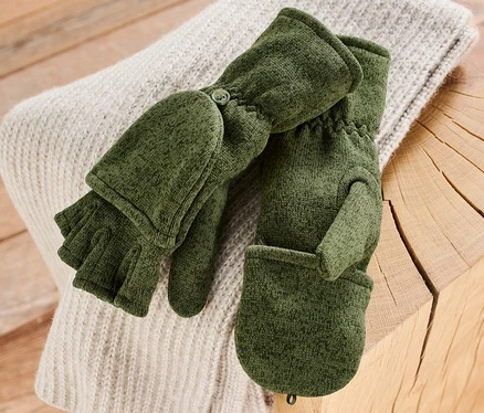 Khaki pletené flaušové palčiaky ležia na svetri na drevenom stole.