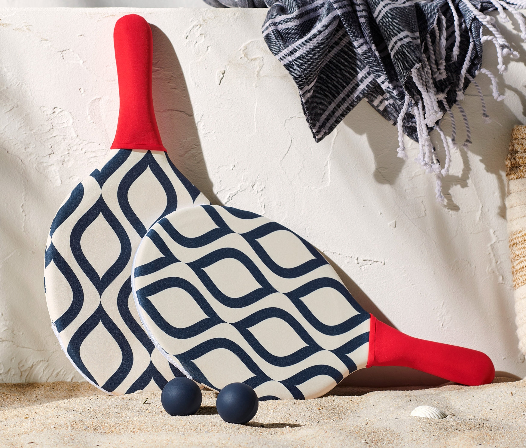 Súprava na plážový tenis leží na piesku vedľa tašky, uteráka a opaľovacieho krému.