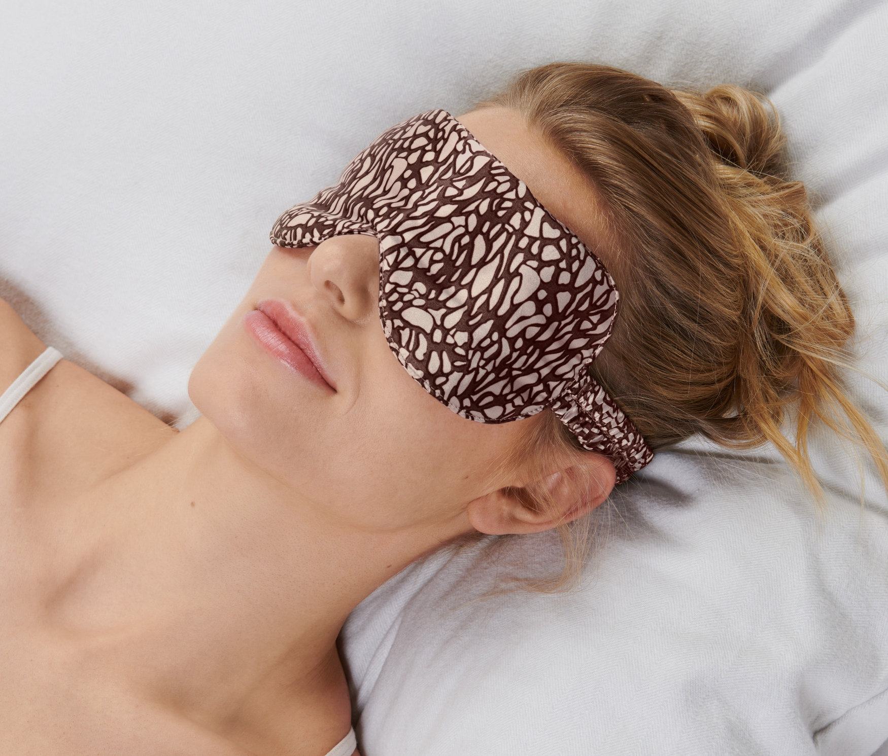 Žena leží na vankúši s maskou na spanie.