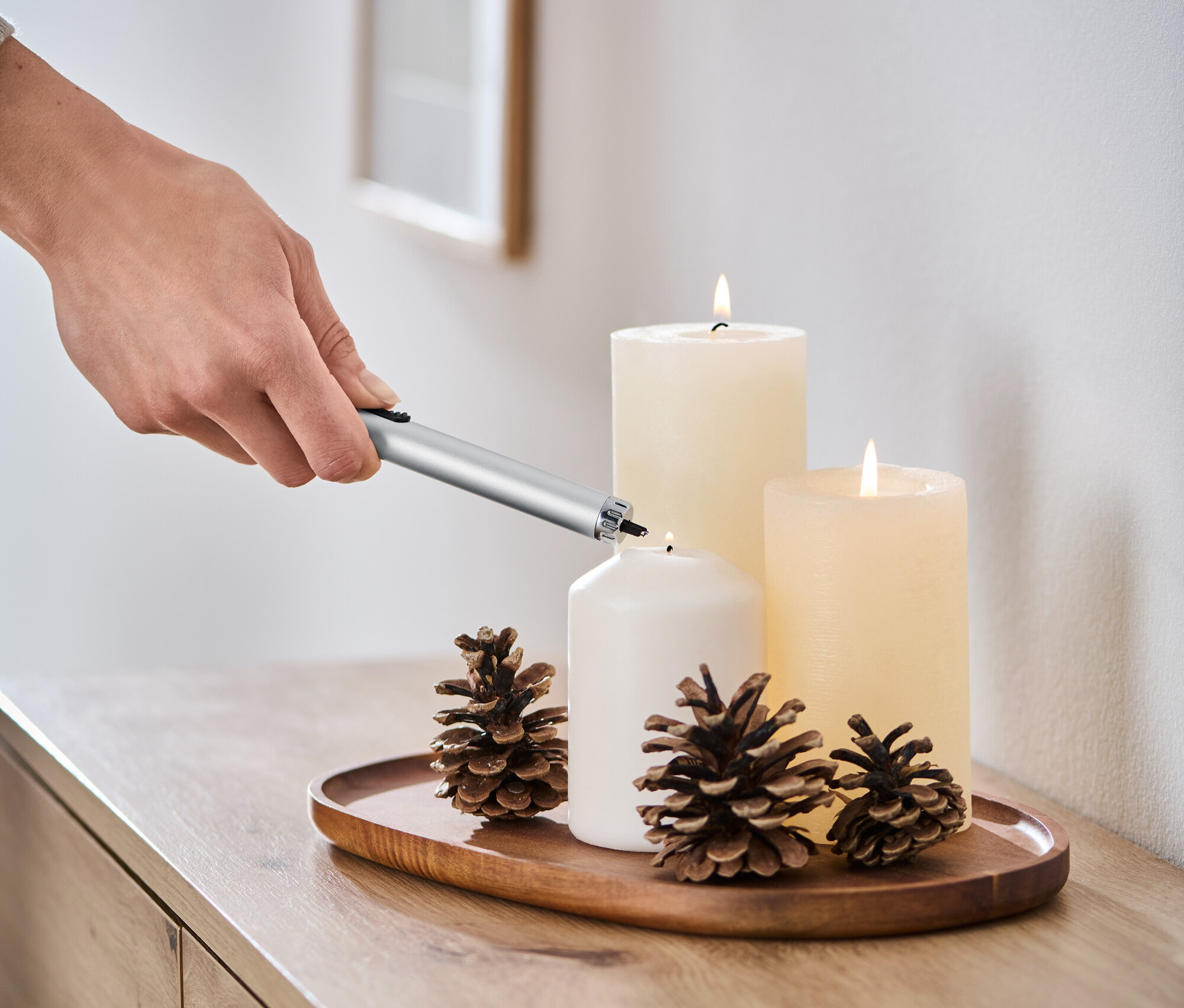 Ruka zapaľuje bielu sviečku pomocou elektrického plazmového zapaľovača.